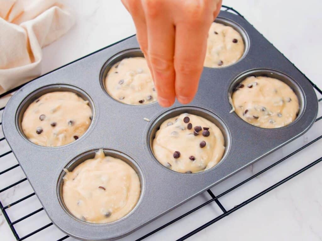 hand adding chocolate chips to muffins in tin