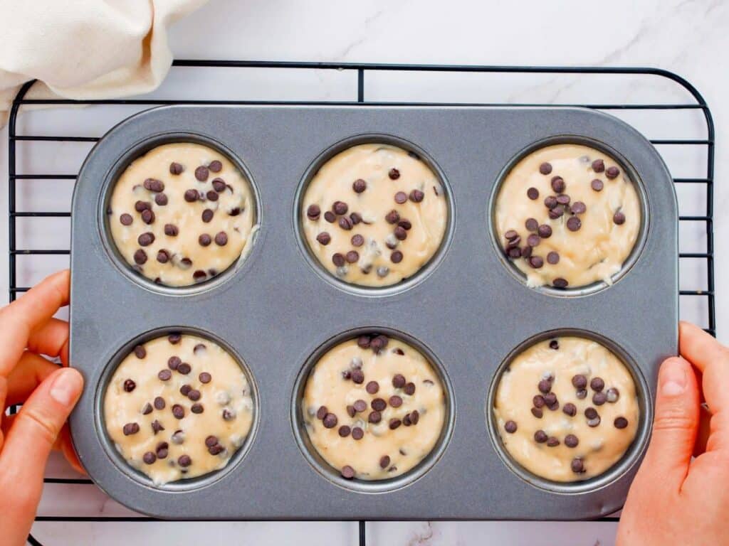 unbaked vegan chocolate chip muffins in baking tin held above wire rack on table