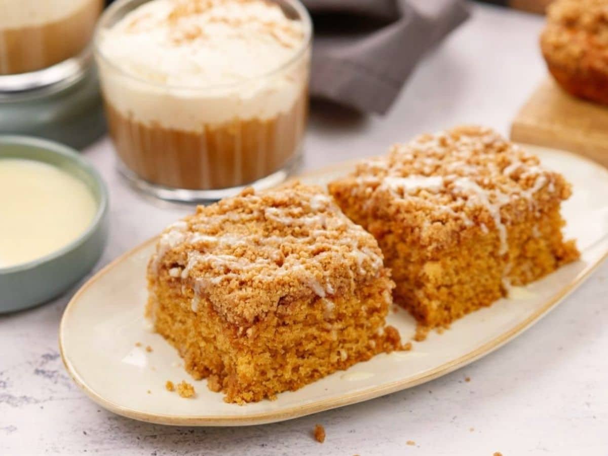 layered latte in glass mug behind plate of sliced vegan coffee cake