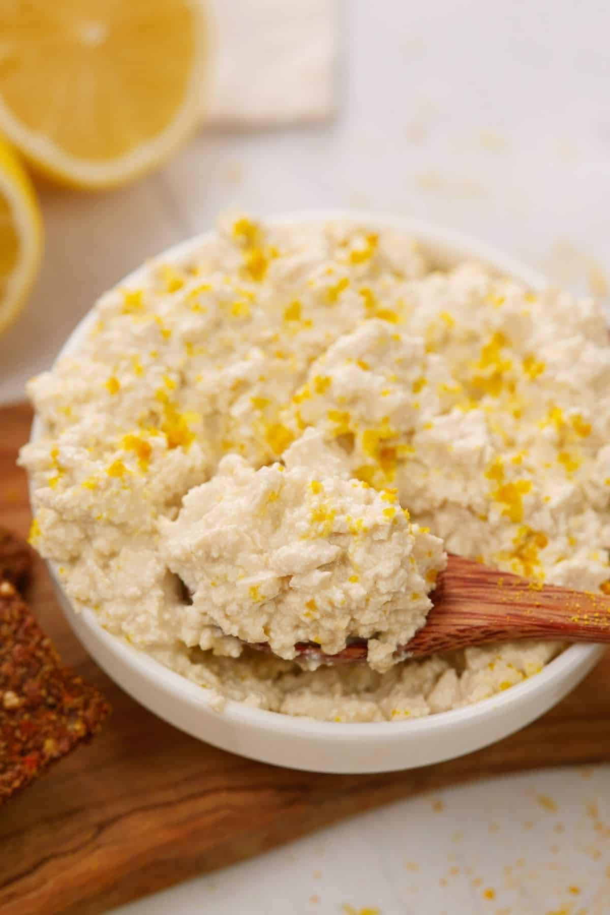 white bowl of vegan cottage cheese sitting on top of wood board