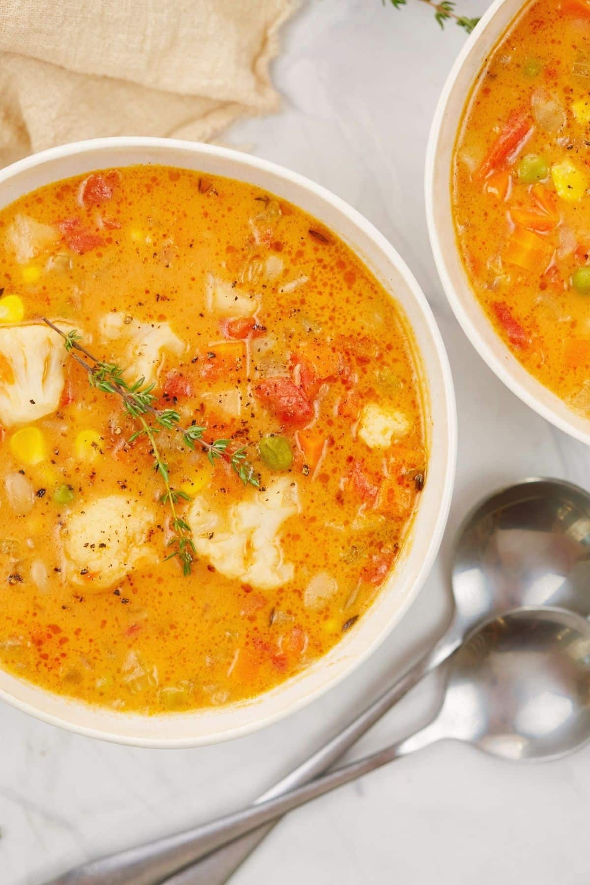 silver spoons on marble beside two white bowls of vegan vegetable soup