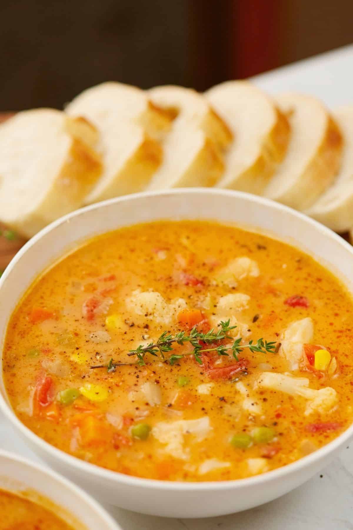 large white bowl of vegan veggie soup beside freshly sliced bread