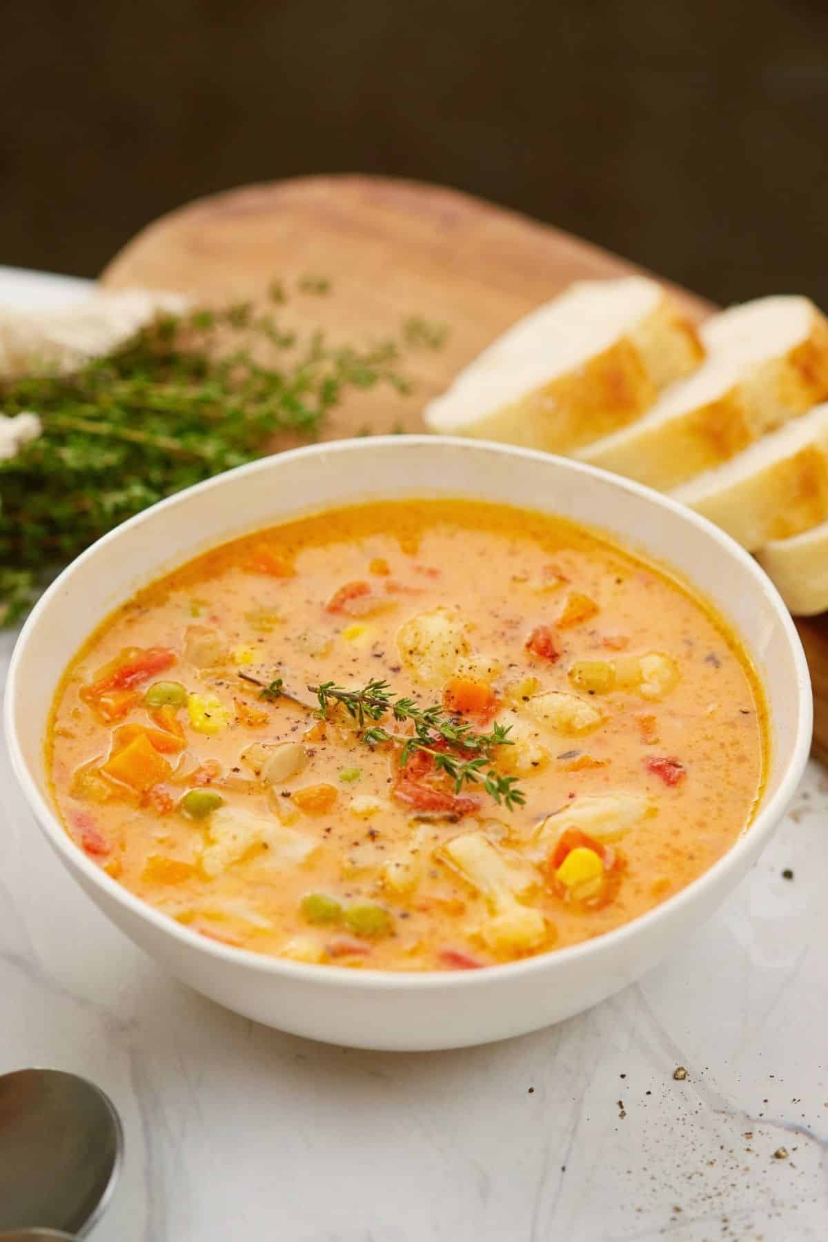 sliced bread on board behind white bowl of veggie soup