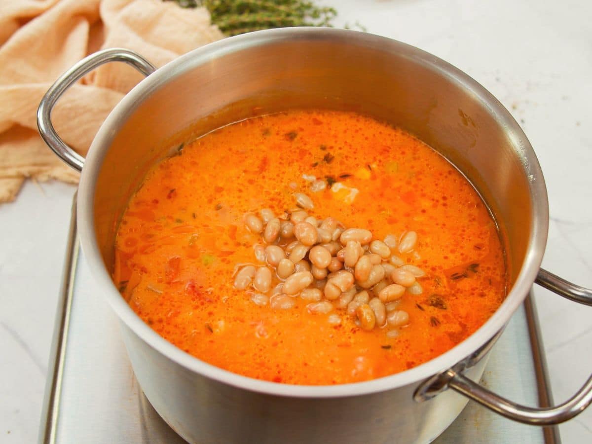 beans being added to soup in stockpot