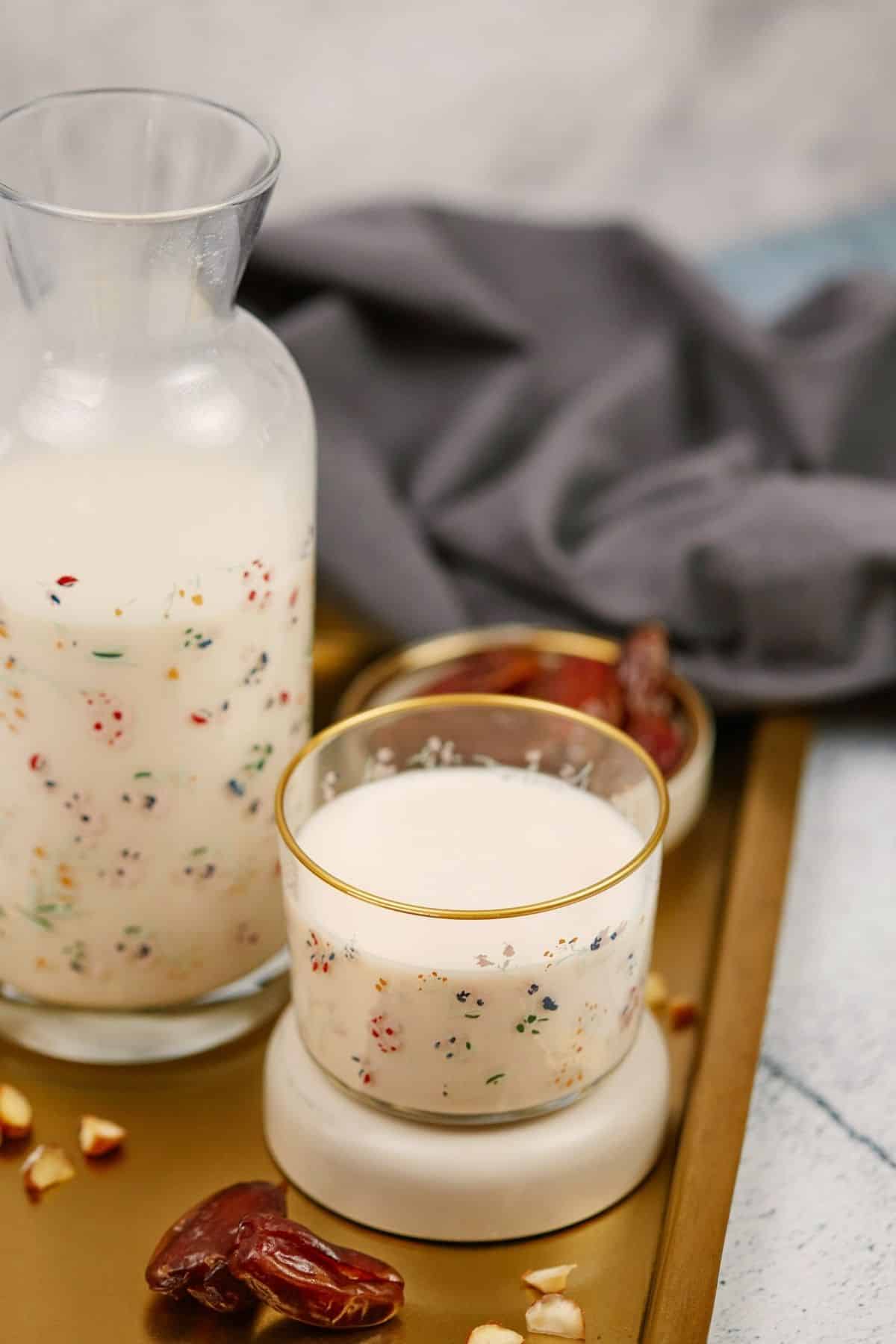 tall glass pitcher on tray holding homemade almond milk recipe next to blue napkin