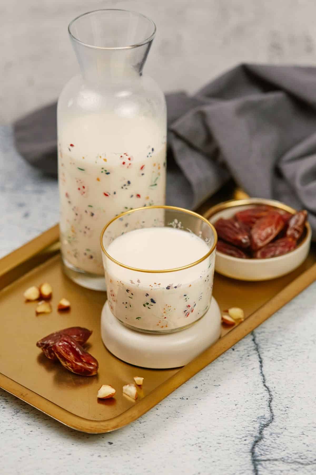wood platter holding almonds next to a glass cup of almond milk