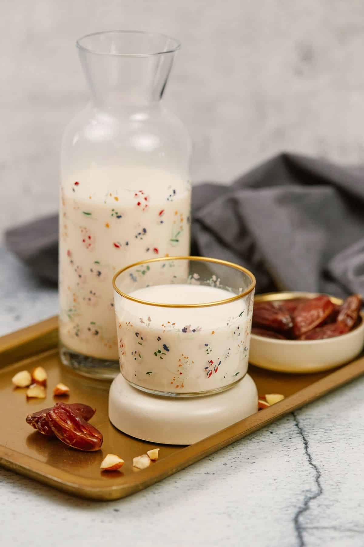 glass jar of almond milk with colorful design on wood tray with small glass of milk