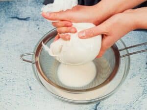 hand squeezing almond milk out of cheese cloth into bowl