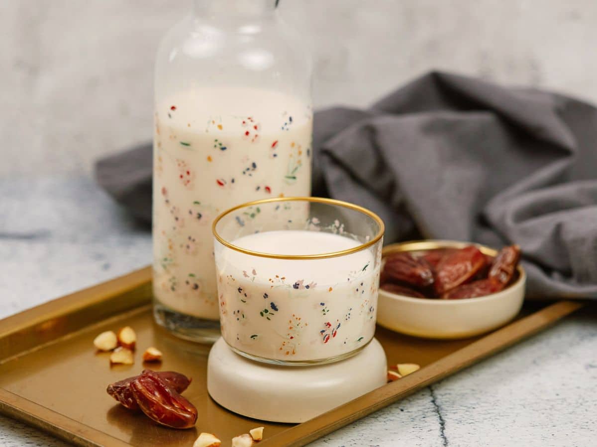 glass jar and cup o milk on wood platter sitting on marble table
