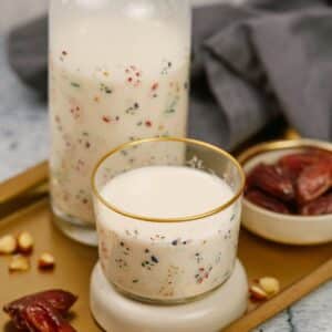 glass jar of almond milk with colorful design on wood tray with small glass of milk