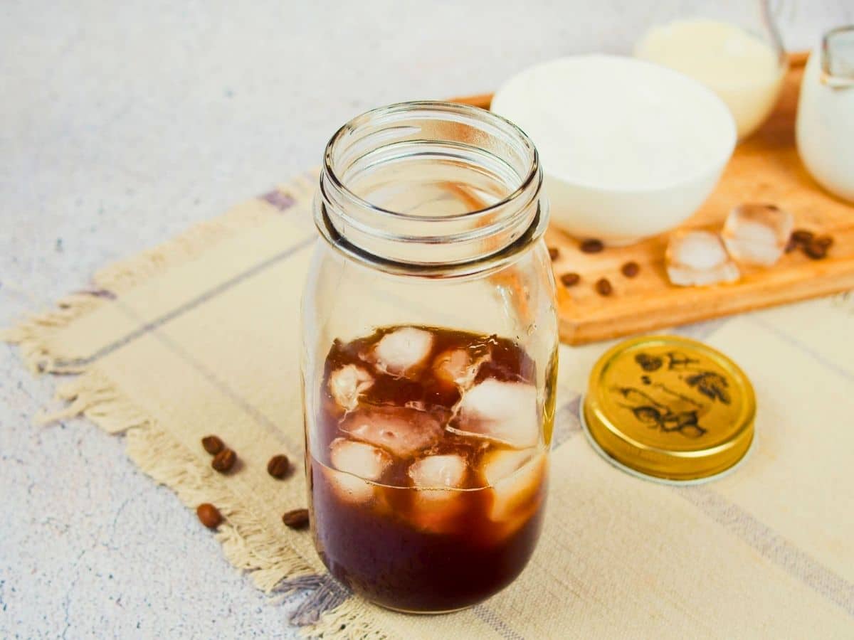 glass mason jar with ice and coffee on tan placemat