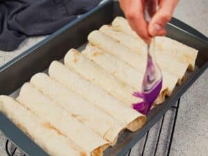 hand brushing oil over top of tortillas in baking sheet