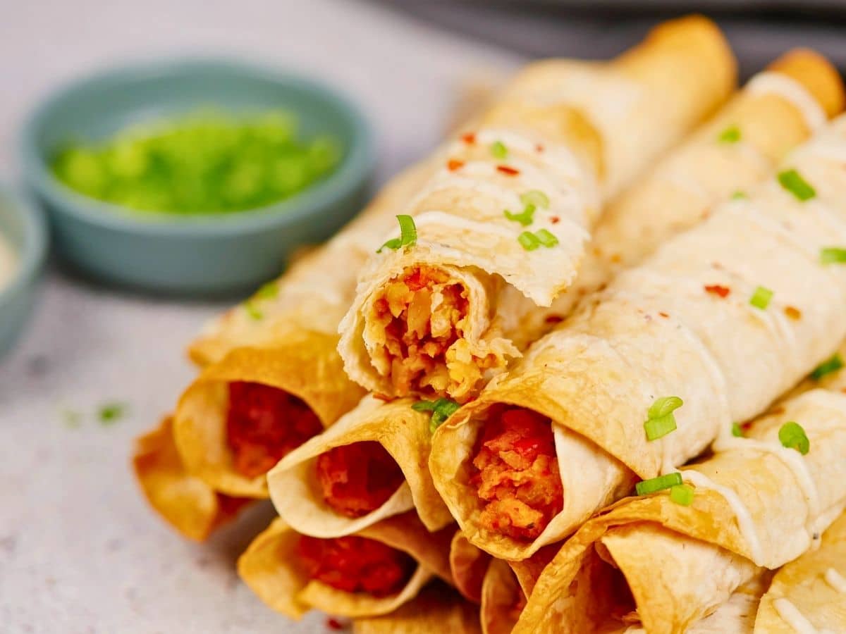 stack of buffalo chickpea taquitos with fresh herbs on top sitting on table