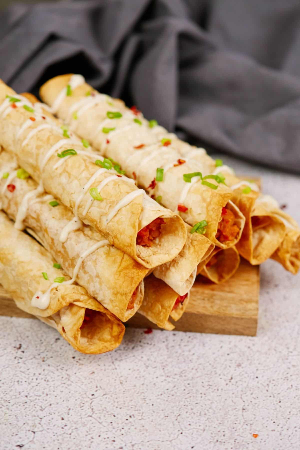 wood platter holding buffalo chickpea taquitos on table by gray cloth napkin