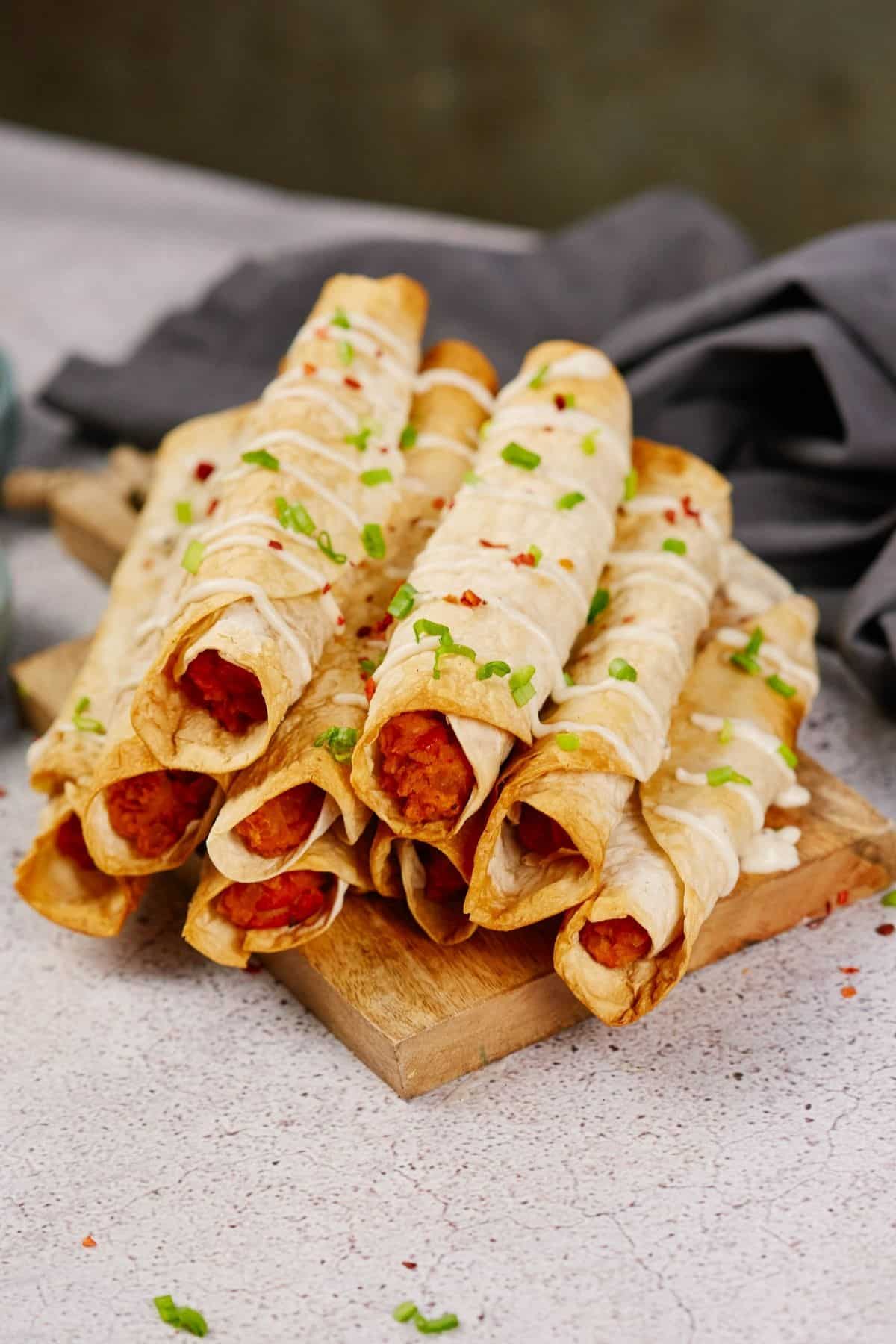 buffalo chickpea sauce peaking out of ends of rolled tacos on wood platter