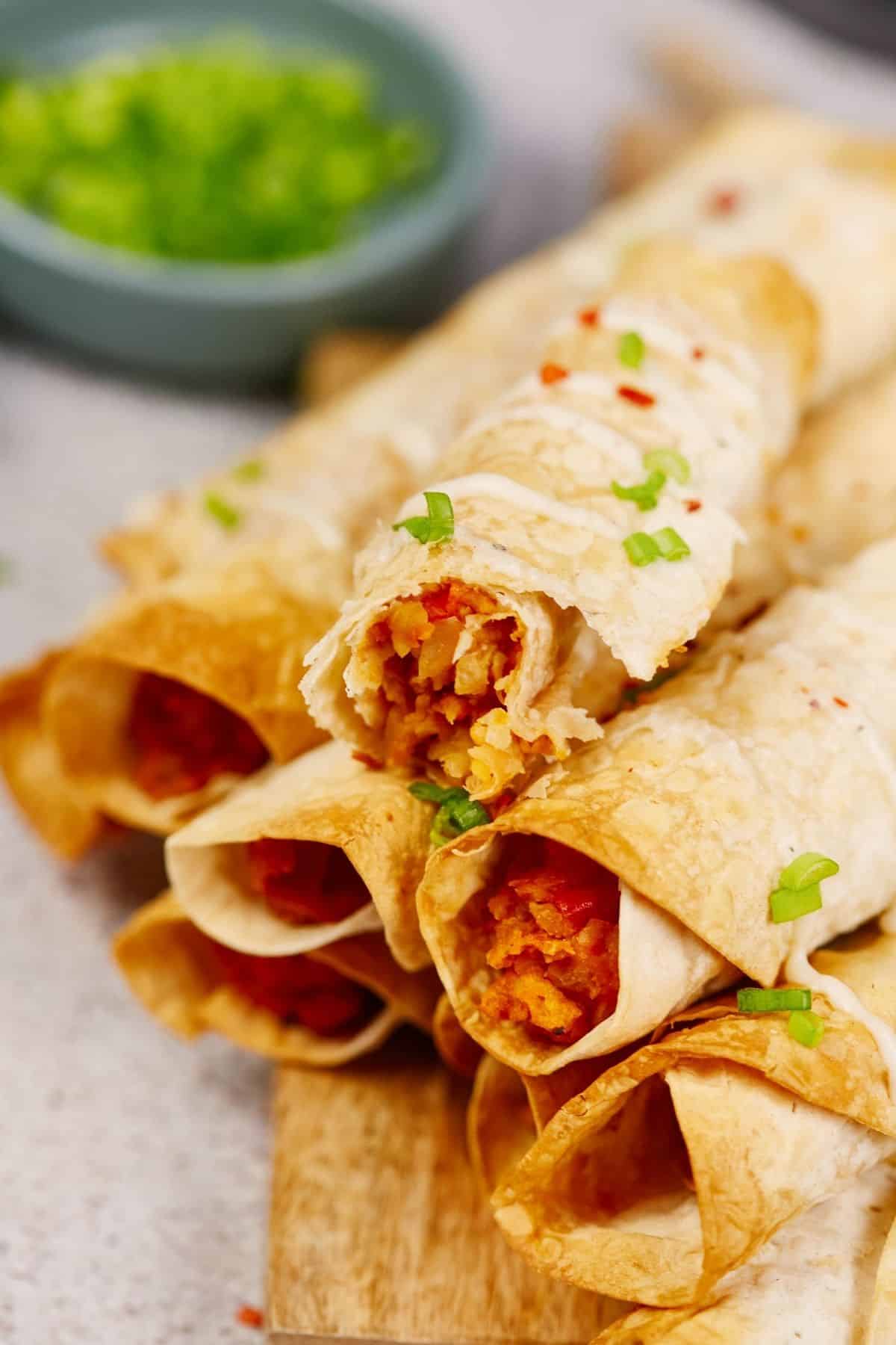 vegan taquitos on top of wood platter by blue bowl of green herbs