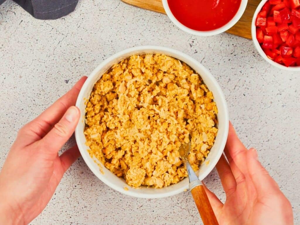 hands holding white bowl of mashed chickpeas