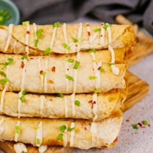 stack of buffalo chickpea taquitos with fresh herbs on top sitting on table