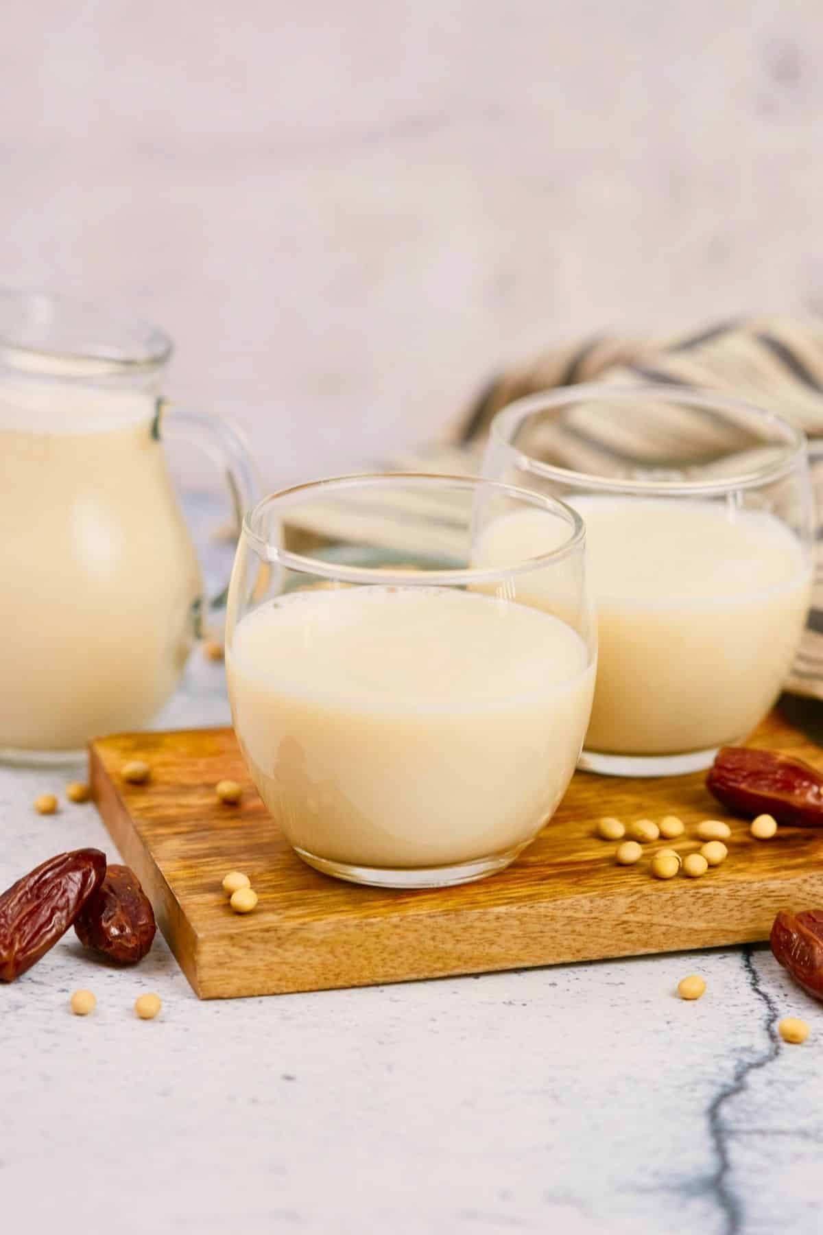 wood platter on marble table topped by cups of milk by glass pitcher of milk