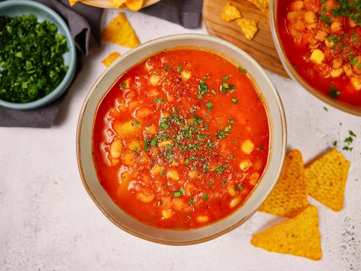 bowl of bean soup on table by bowl of cilantro and tortilla chips