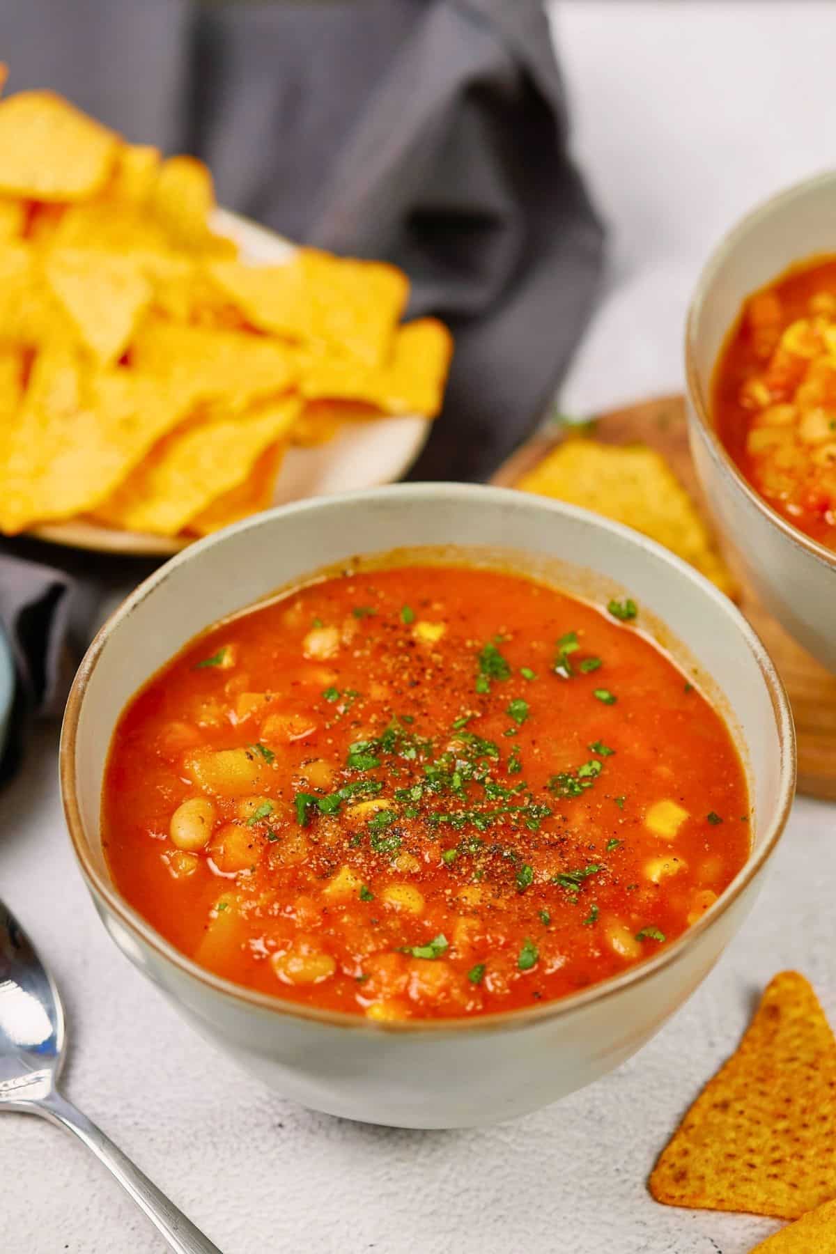 chips on gray napkin behind green bowls of soup