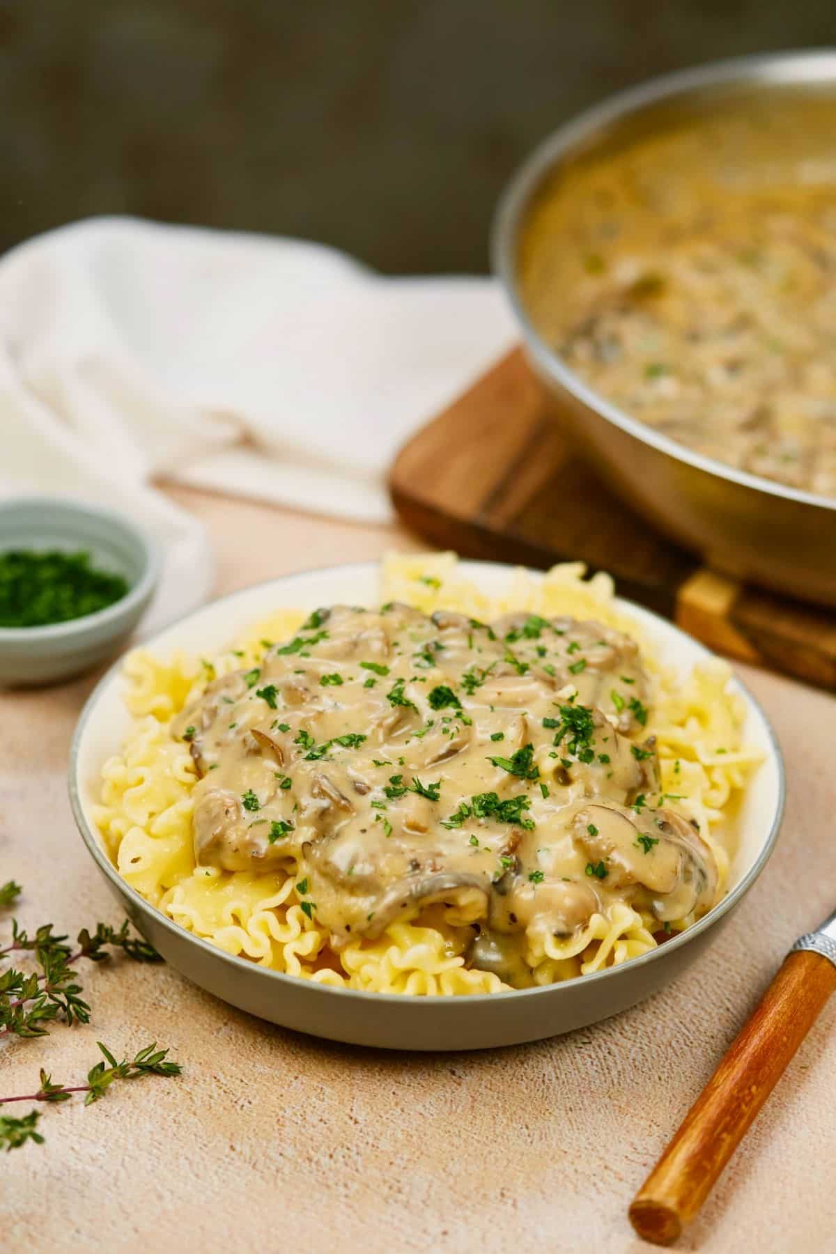 bowl of vegan stroganoff on table by skillet of mushroom sauce