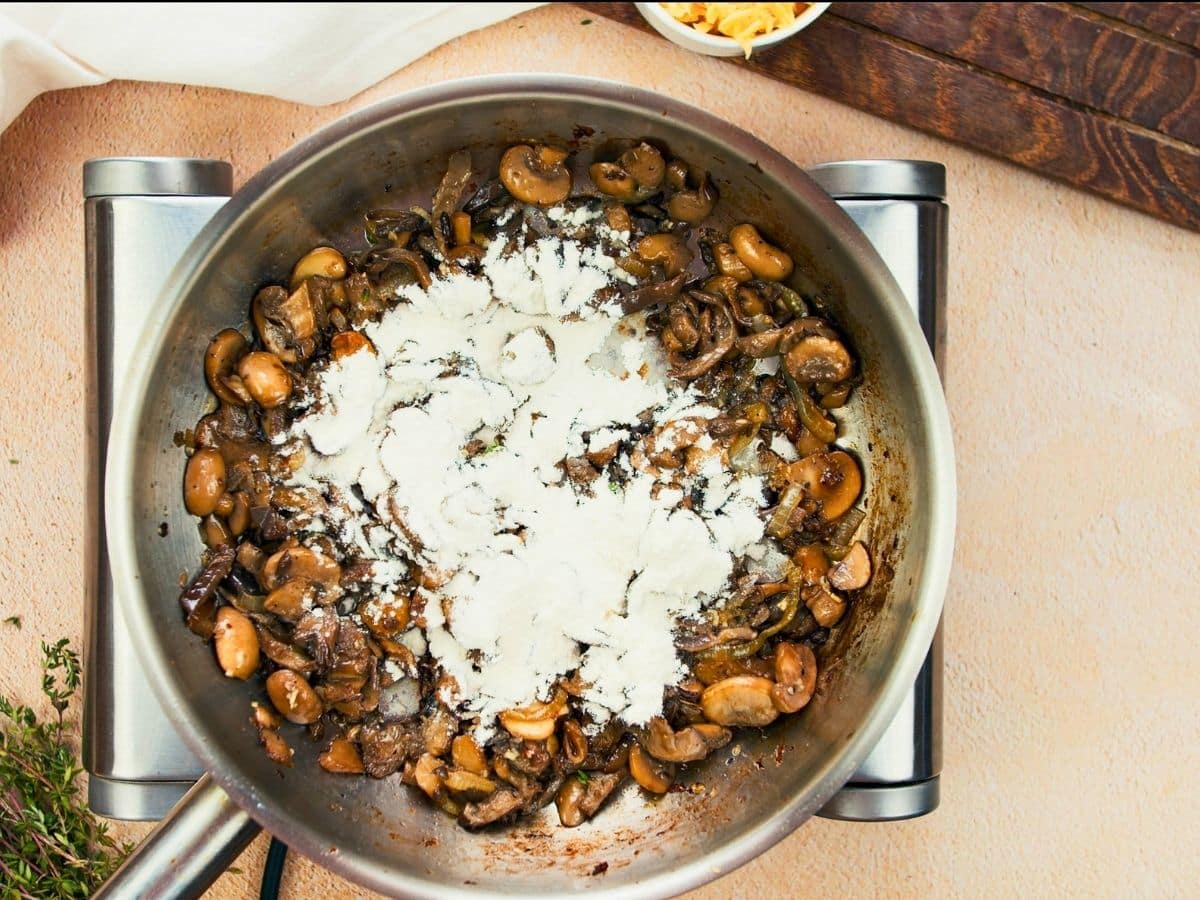 flour on top of mushrooms in skillet on hot plate
