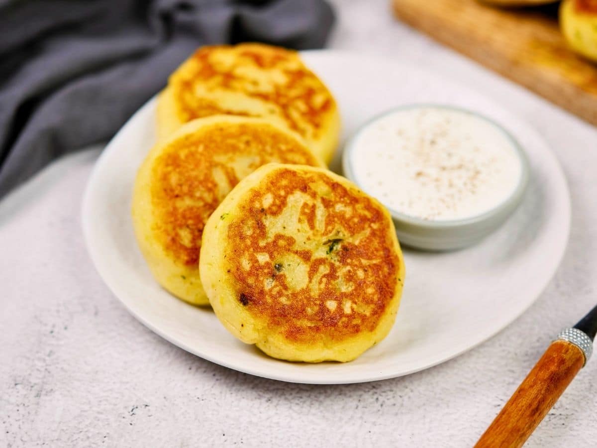 round white plate with 3 stuffed potato cakes and small bowl of creamy dipping sauce