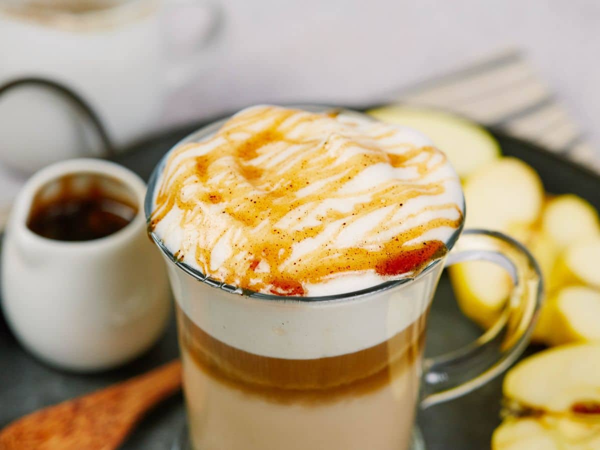 glass mug filled with vegan apple crisp macchiato sitting on tray by sliced apples