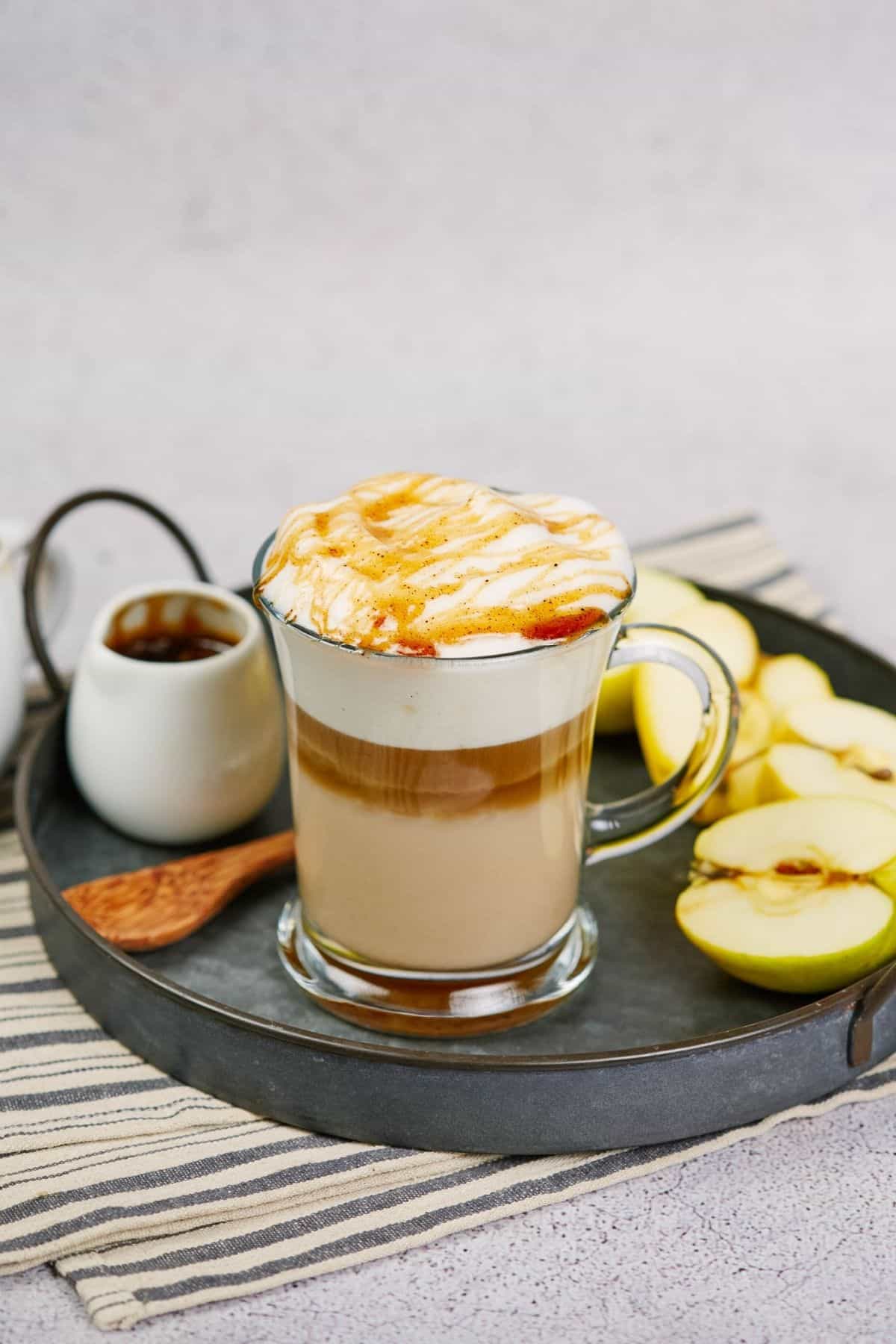 coffee and apples on round gray tray on striped napkin on table