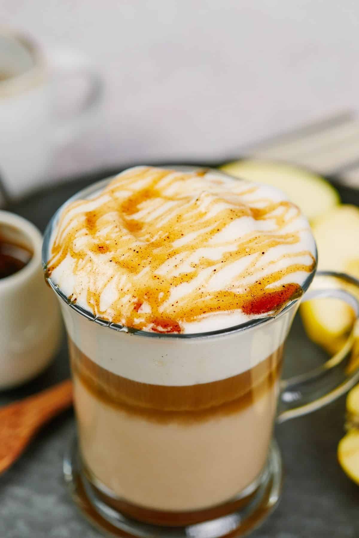 syrup drizzled on top of foam on apple crisp macchiato in glass mug