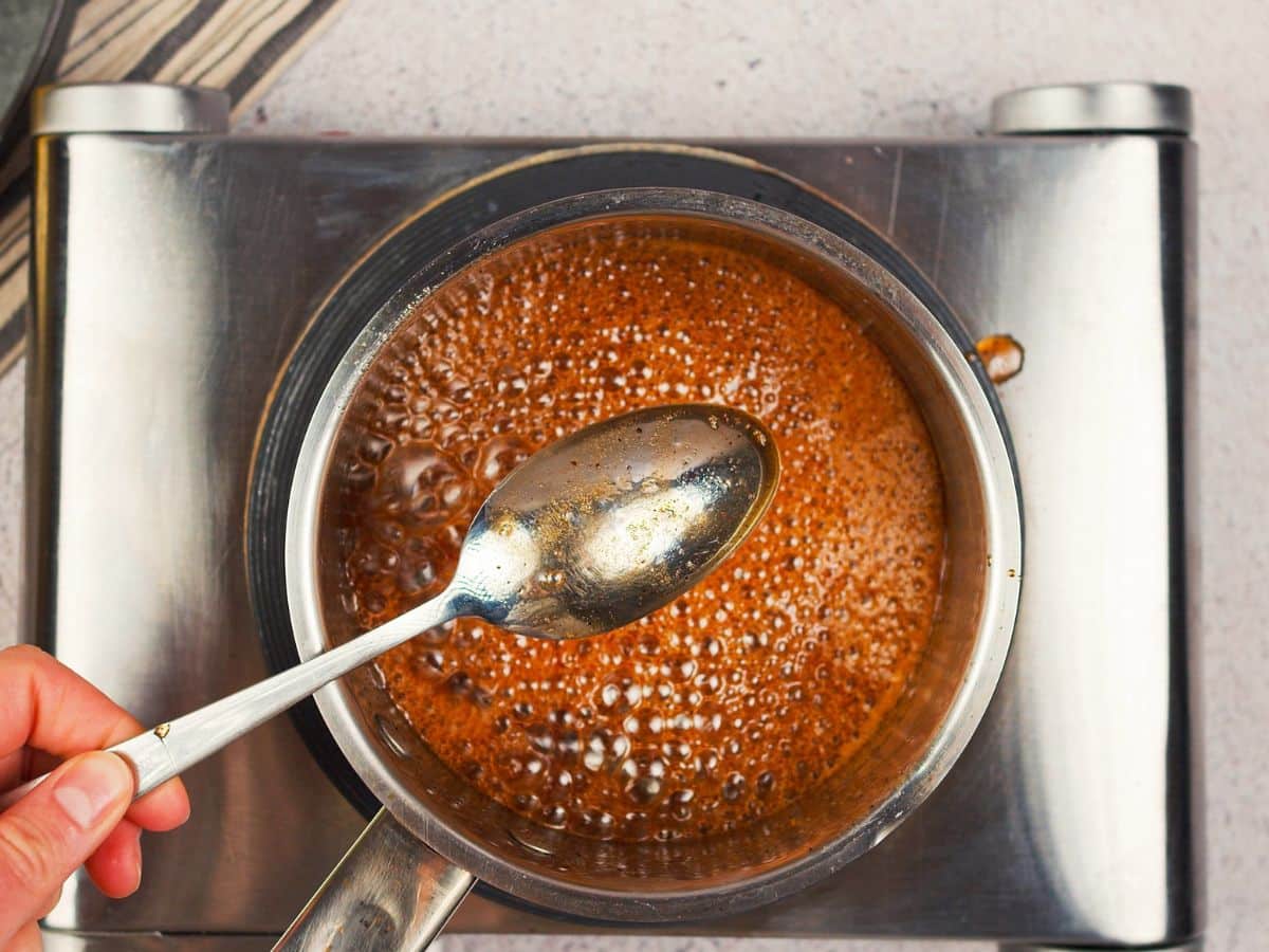 boiling brown liquid in saucepan with spoon held above