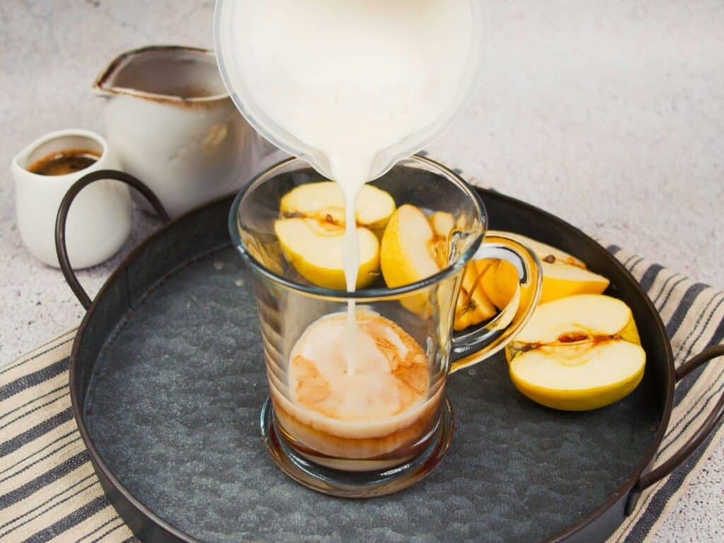 glass mug on gray platter with milk being poured over coffee and syrup
