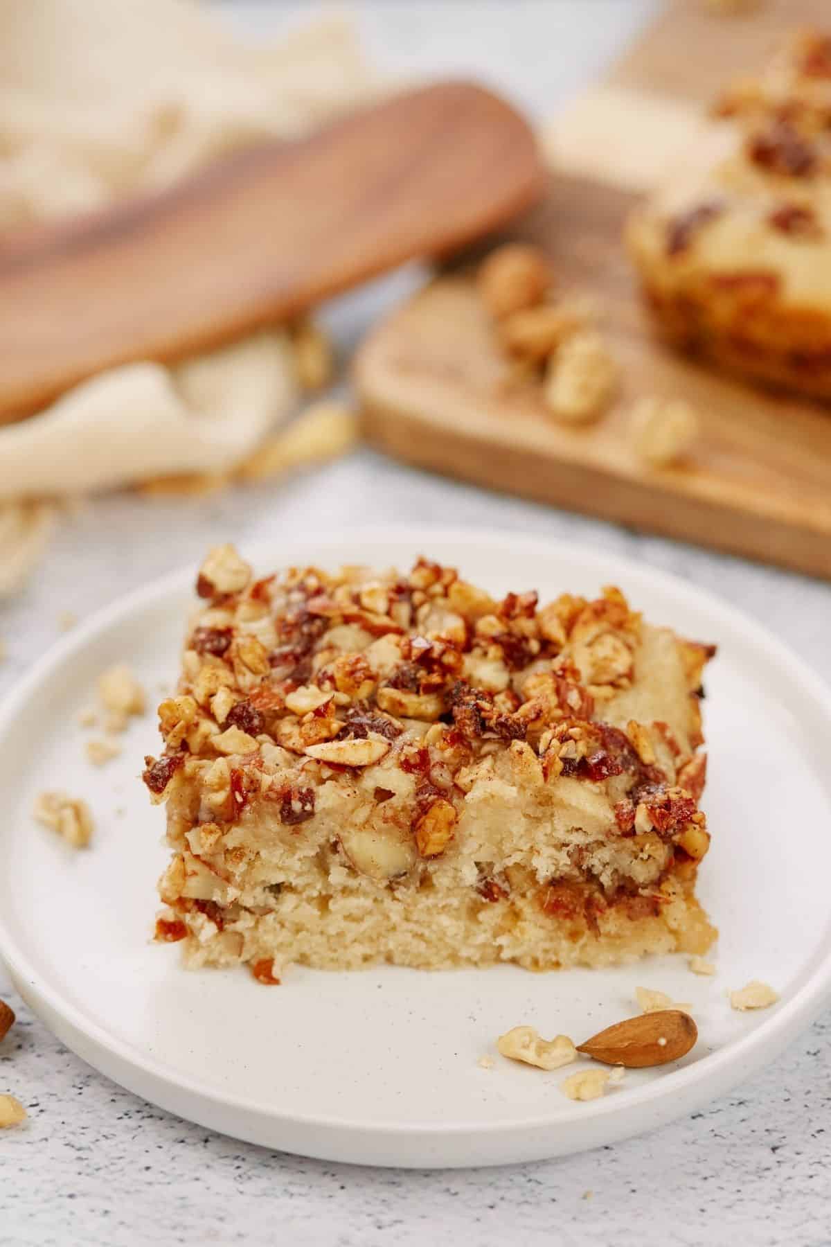 round white saucer with slice of cake topped by nuts on table by wooden cutting board