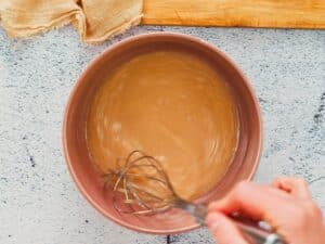 whisk in brown bowl of egg and sugar mixture