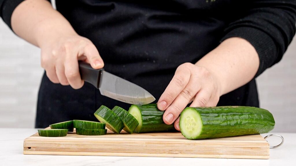 cucumber being sliced on cutting board