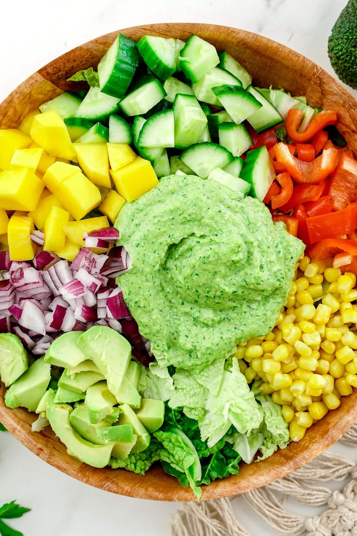 colorful salad with creamy green dressing in large wood bowl on table