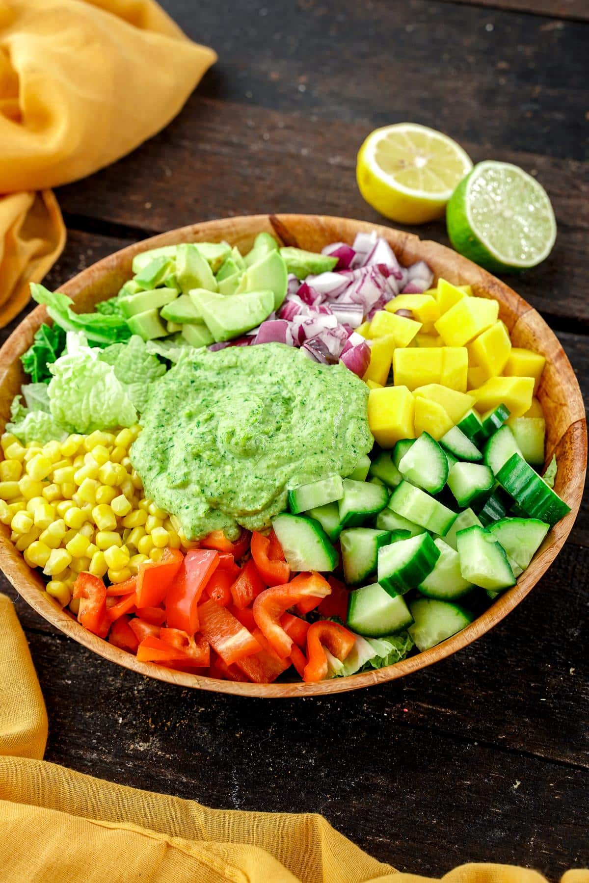 wooden bowl of avocado mango salad on wood table by yellow napkins