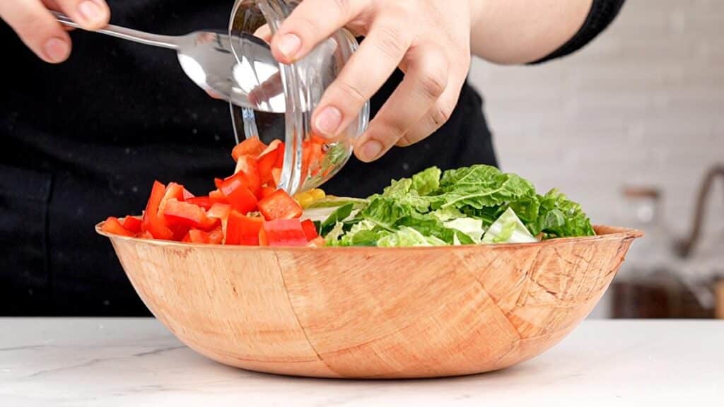 ingredients for avocado mango salad being poured into wooden bowl