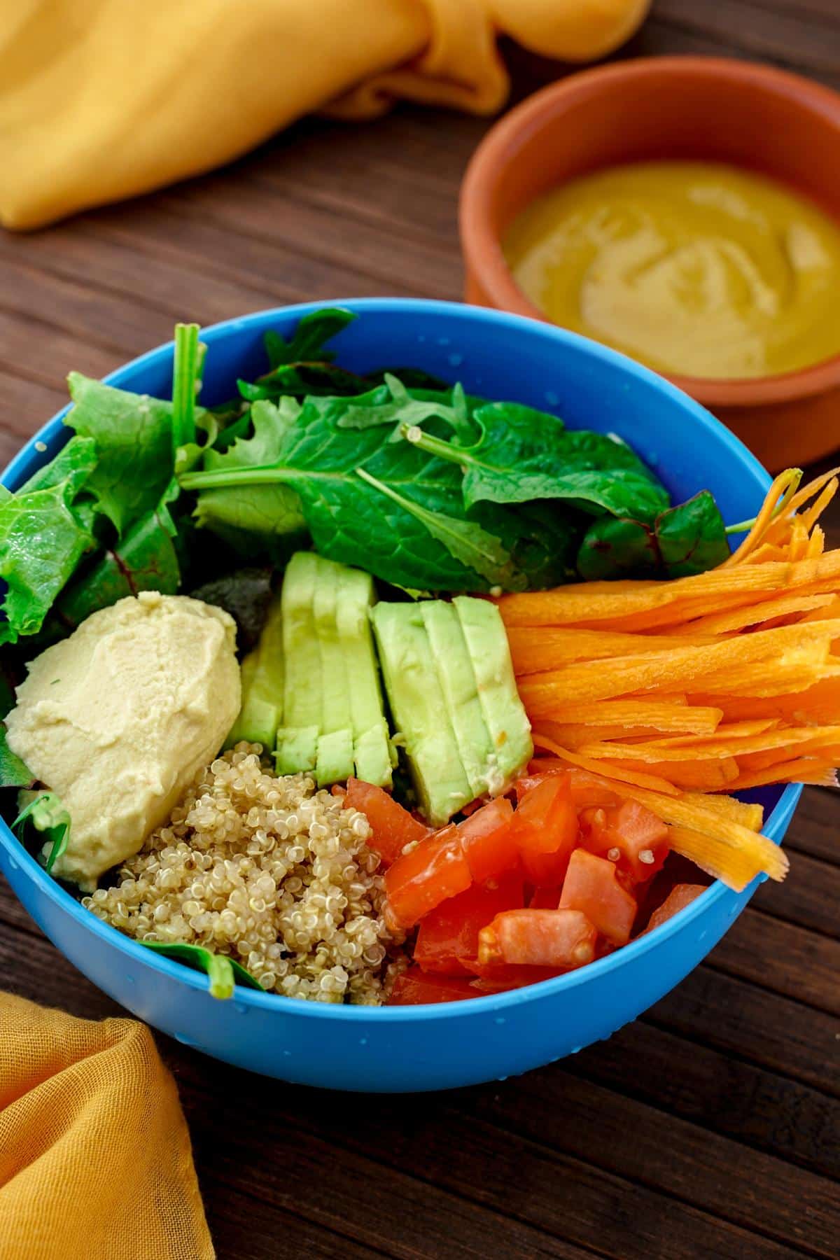 carrots, avocado, hummus, quinoa, tomato, and lettuce in blue bowl on wood table