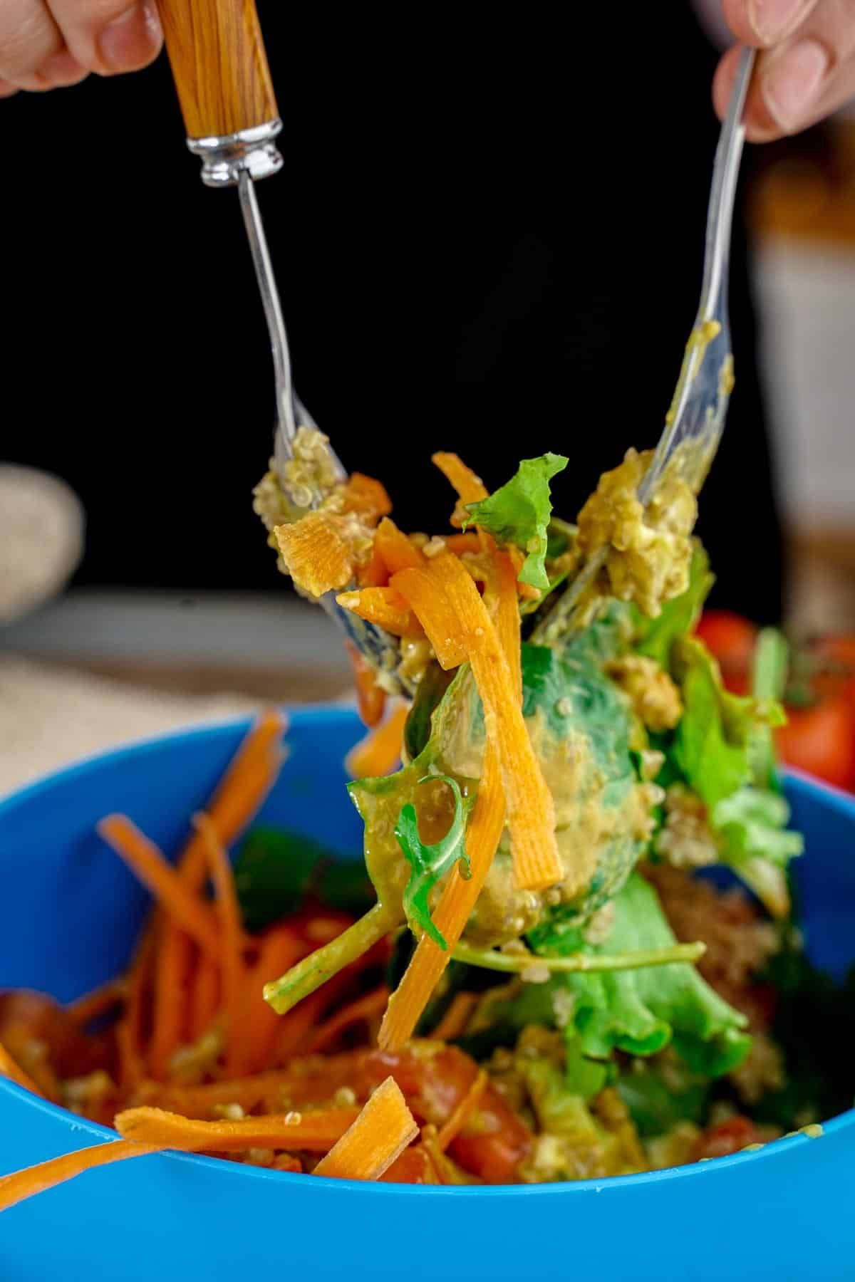 two forks holding up salad out of blue bowl