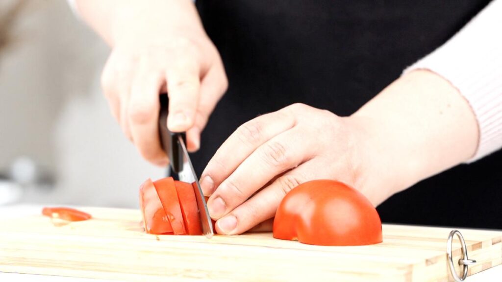tomato being sliced on wood cutting board