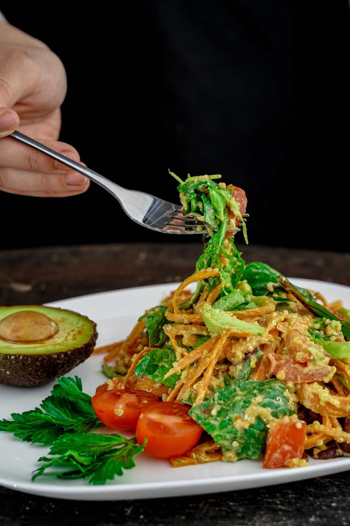 fork of salad held above white plate with black background