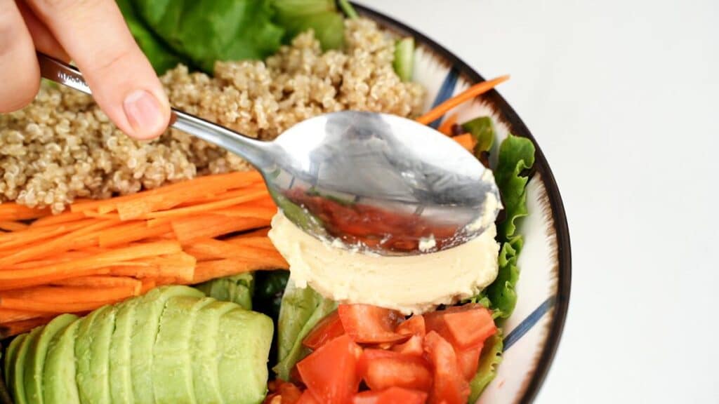 hummus being spooned on top of tomatoes in bowl of salad