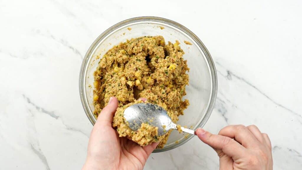 spoon of chickpea mixture being formed into a patty above glass bowl