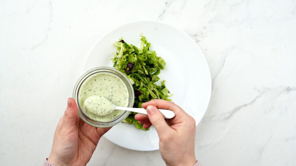 dressing being spooned over bed of lettuce