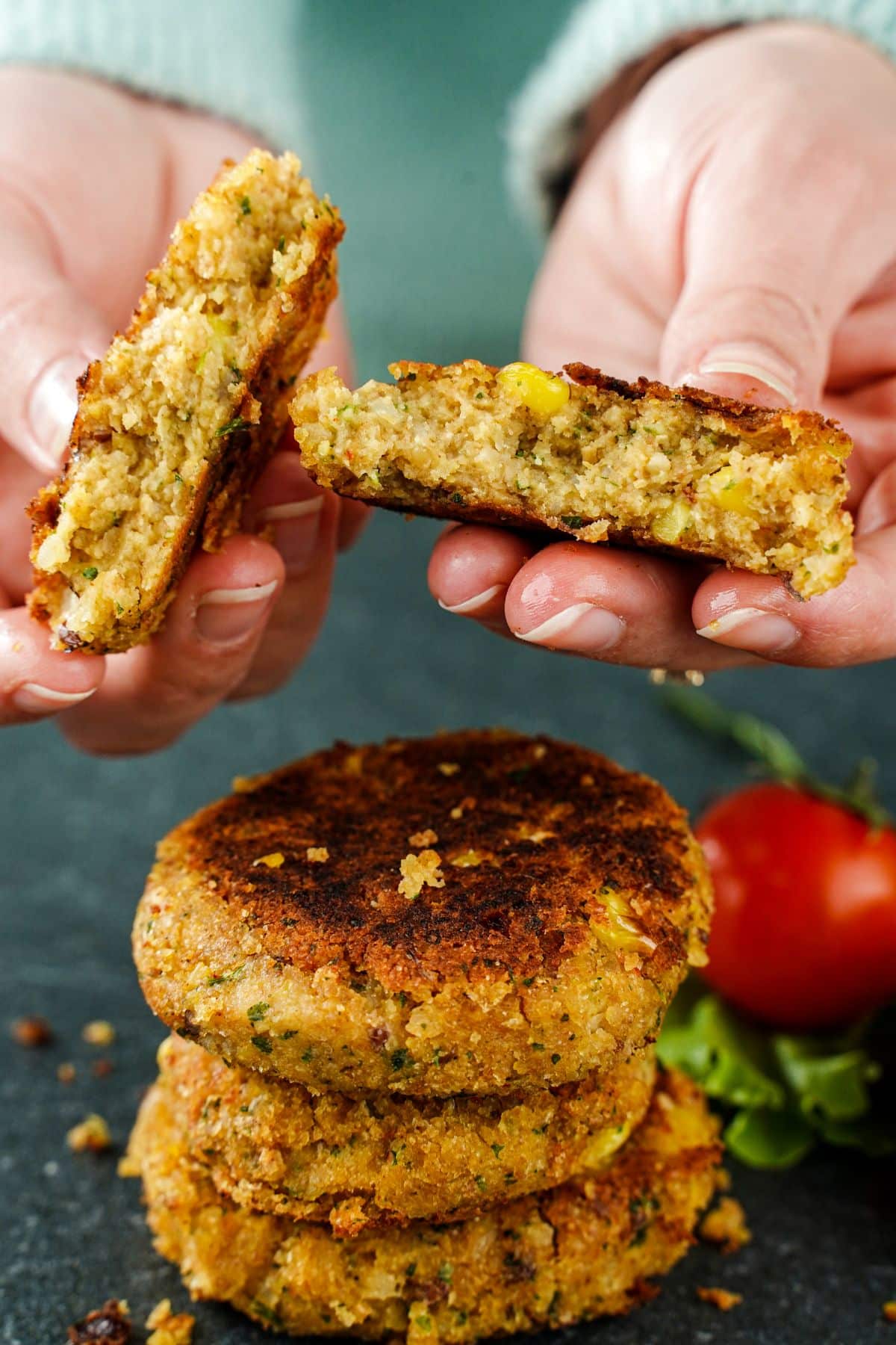 hand holding chickpea corn patty that is pulled apart above stack of patties