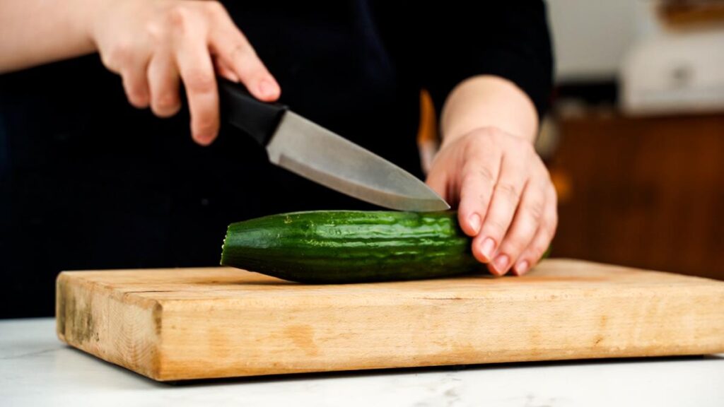 cucumber being sliced on cutting board