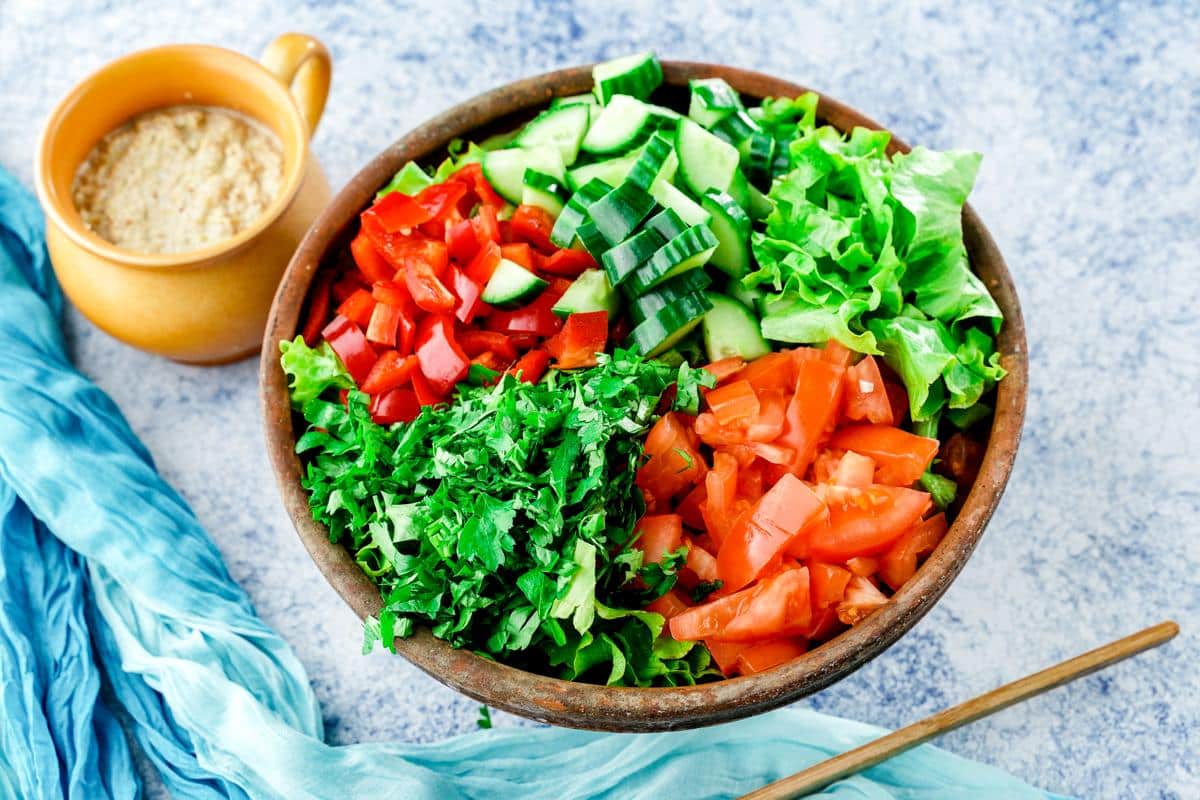 wooden bowl of salad on blue placemat with yellow mug of dressing on side