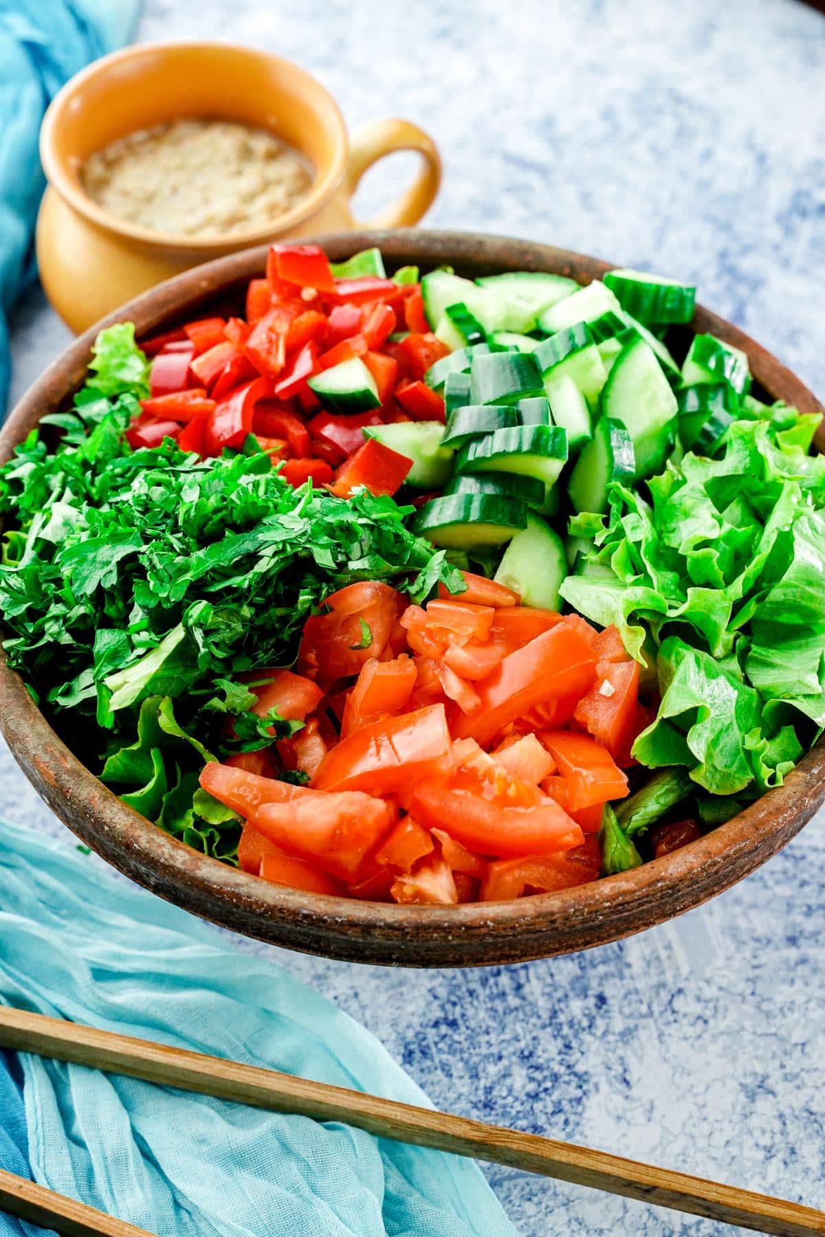 wood bowl of salad on blue and gray table with dressing in background